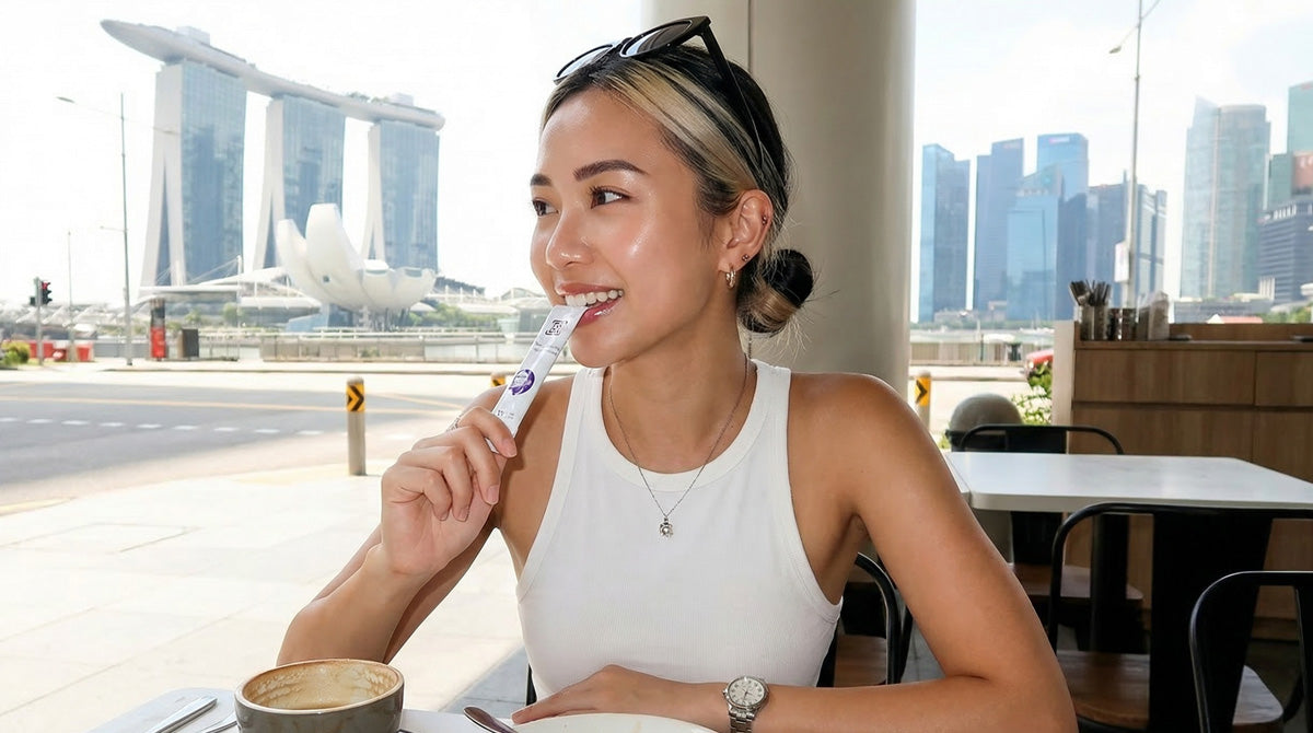 A candid, sunlit photo of a woman at a Singapore cafe with the Marina Bay Sands background, smiling while enjoying a sachet of the Halal-certified YoungLong Berry White supplement as part of her daily beauty routine.