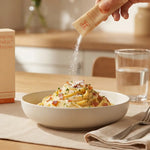 Sprinkling digestive enzyme powder over creamy pasta for enhanced digestion and vitality