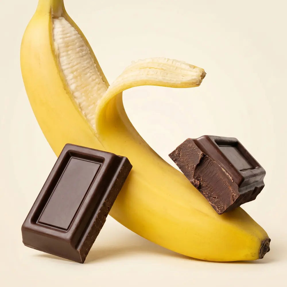 Peeled banana with two pieces of dark chocolate against a light background