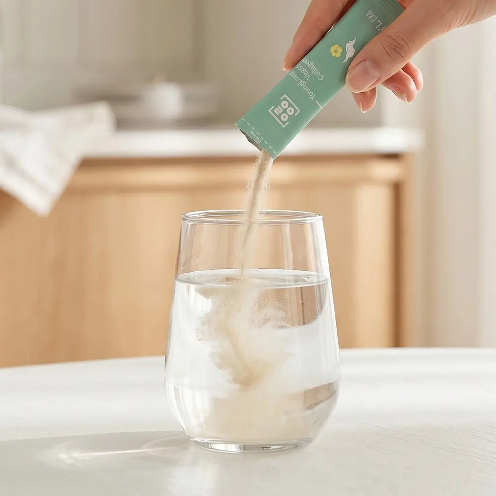 Hand pouring vegan collagen supplement powder into glass of water for daily wellness